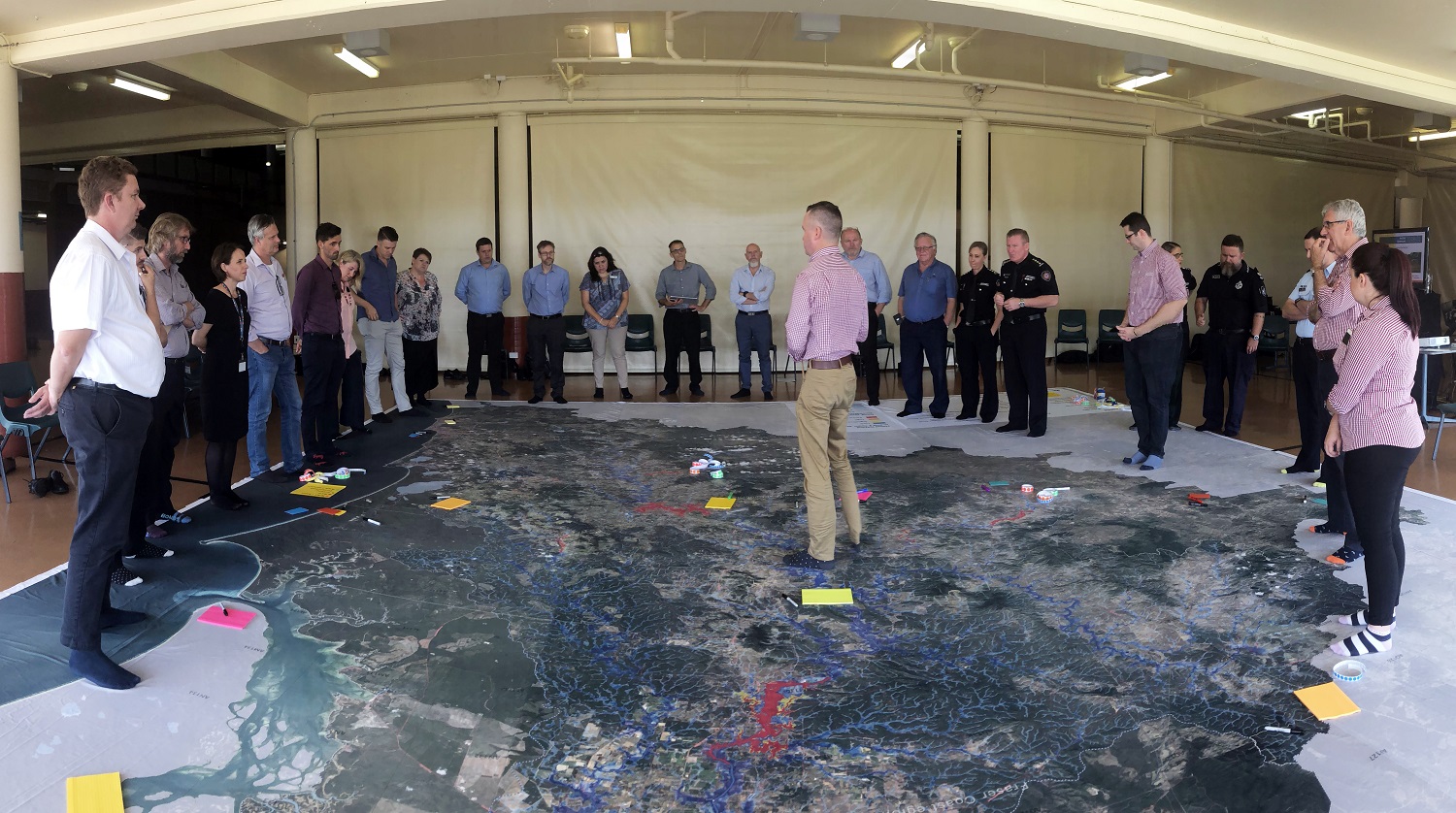 Man standing on very large map talking to about 20 people