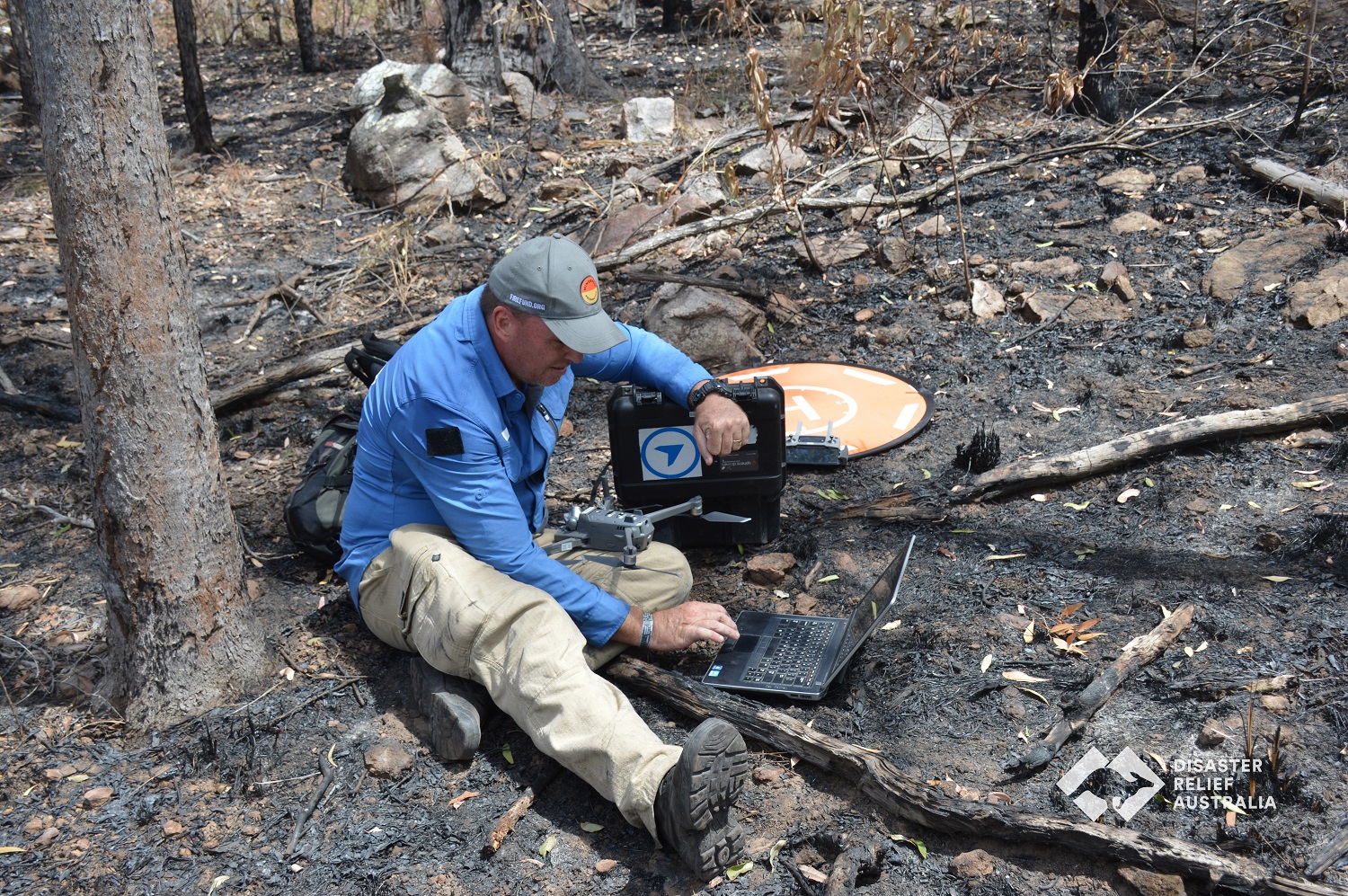 Man sitting on ground in burnt forest with drone and related gear