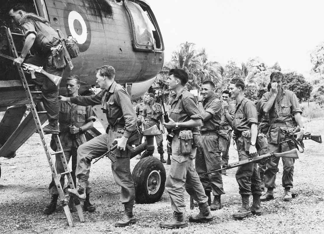 Half a dozen or so soldiers board a helicopter in the jungle