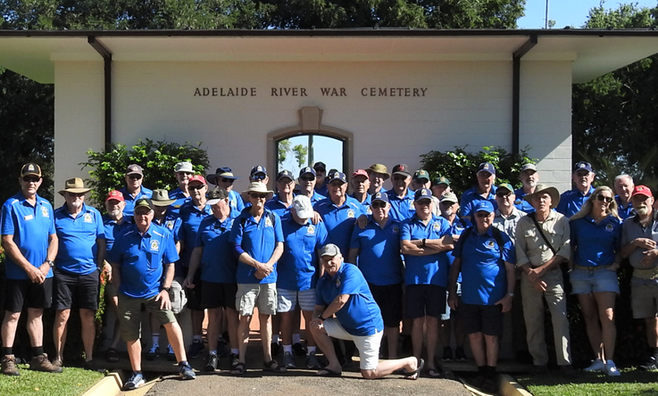 Forty or fifty men in blue T-shirts in group photo at entrance to Adelaide Creek War Cemetery