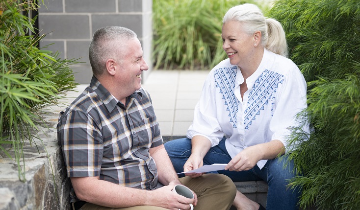 An ageing couple chat on steps in a back garden