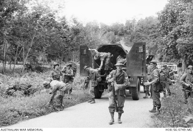 Soldier faces camera while around 10 others move around armoured truck