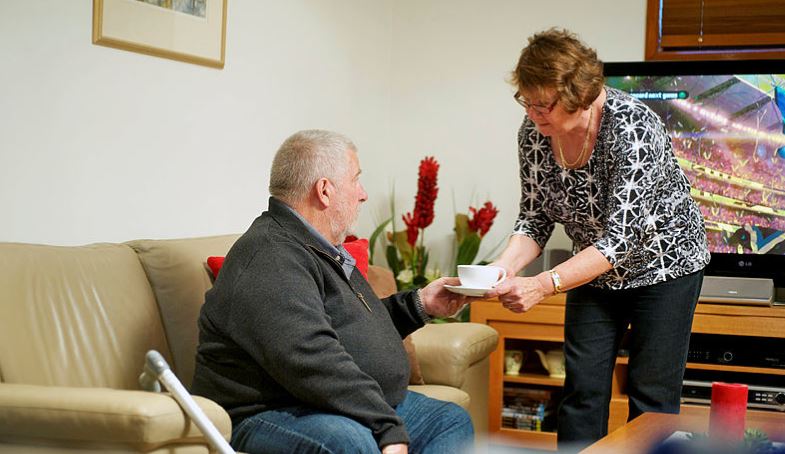 Woman serves tea to ageing man on sofa