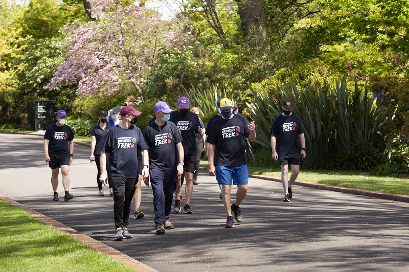 Several men wearing Open Arms T-shirts walking down a path in what looks like a park