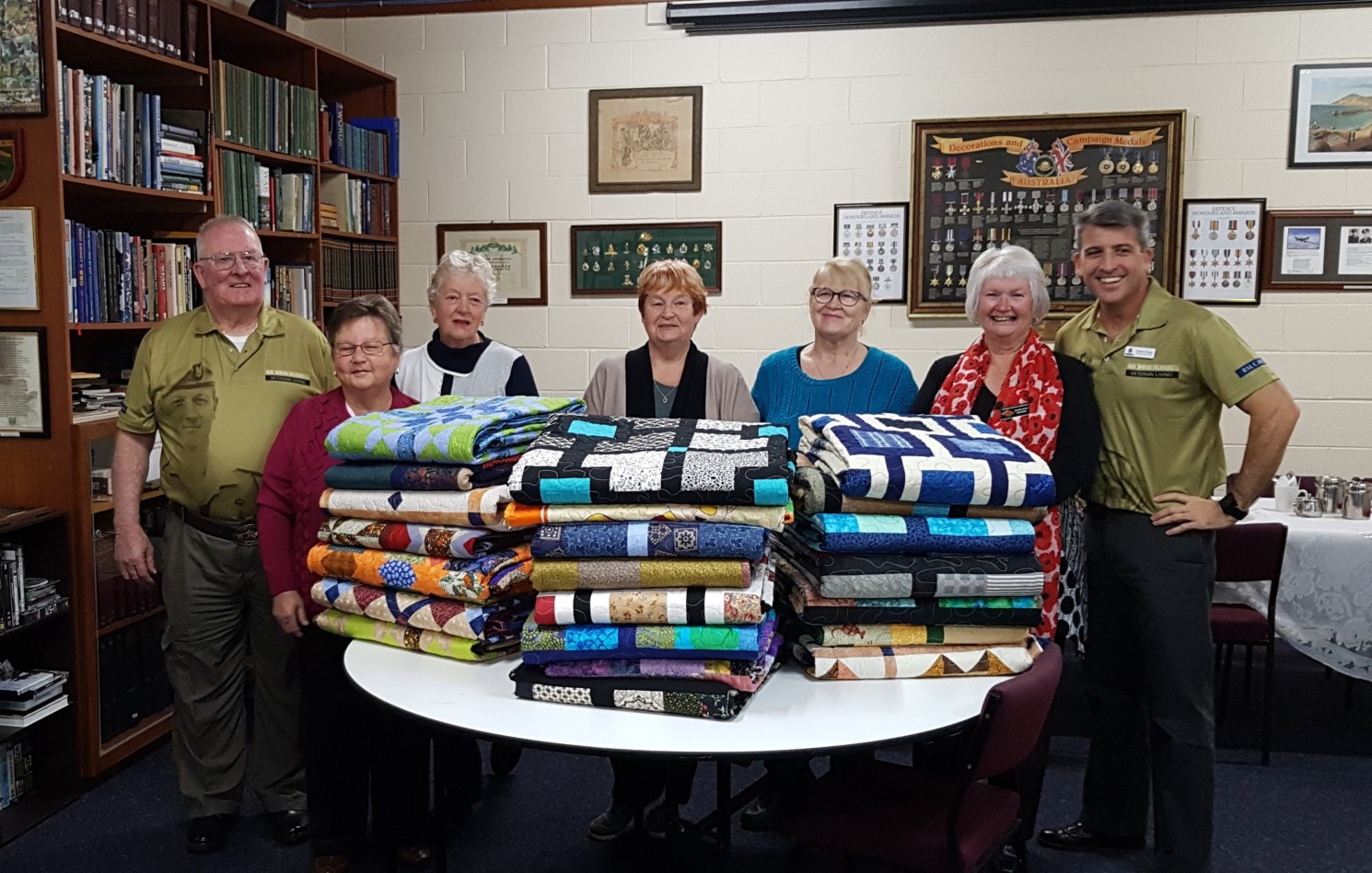 A group of people standing behind a table that holds folded patchwork quilts