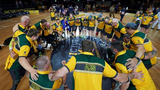 A ring of basketballers gather together in a huddle on a basketball court or similar