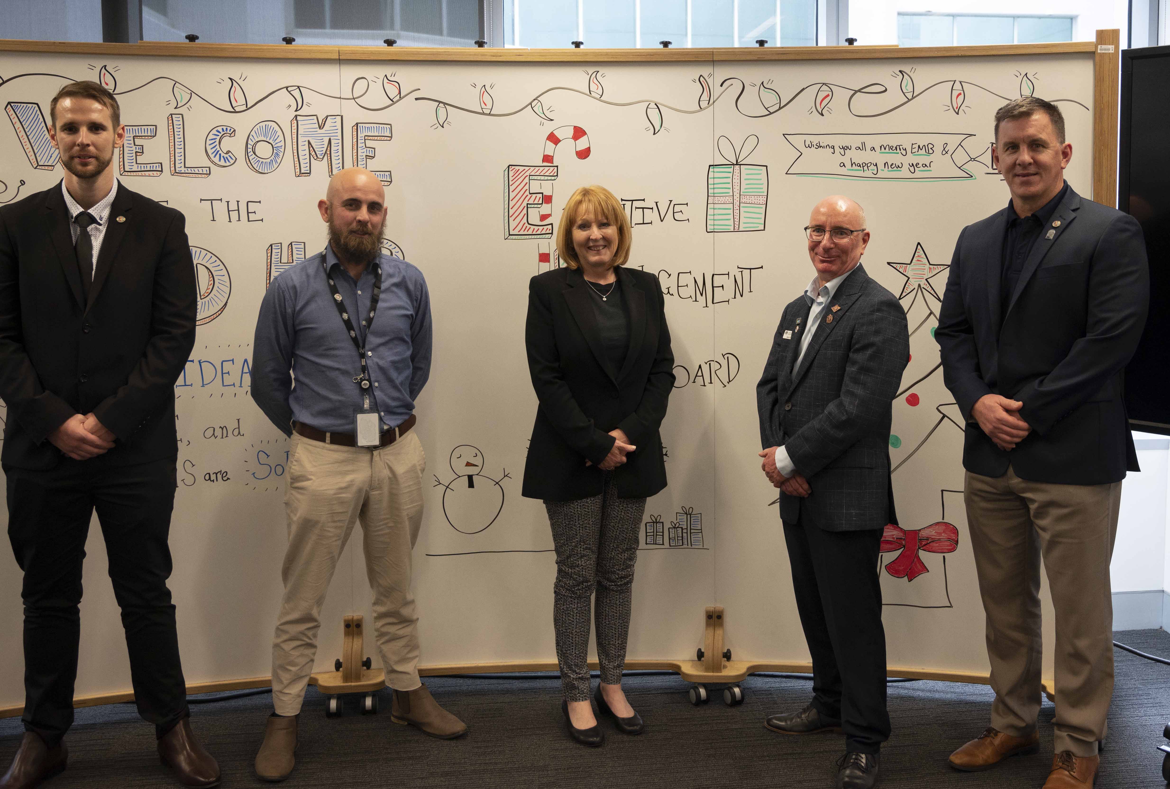 A woman and four men posing in front of a white board