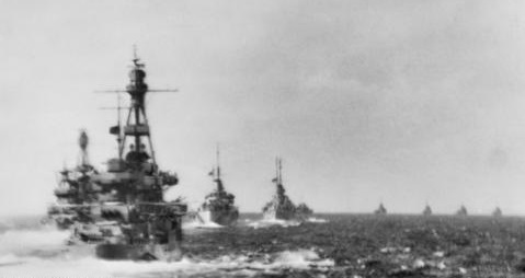 Grainy black and white photo of five warships sailing in a column
