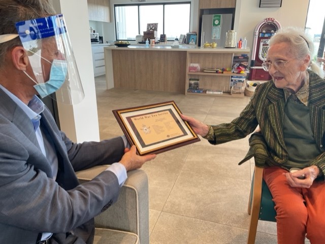 Man in face mask hands certificate to elderly woman