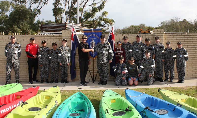 Men and children, mostly in naval uniform, pose in front of kayaks