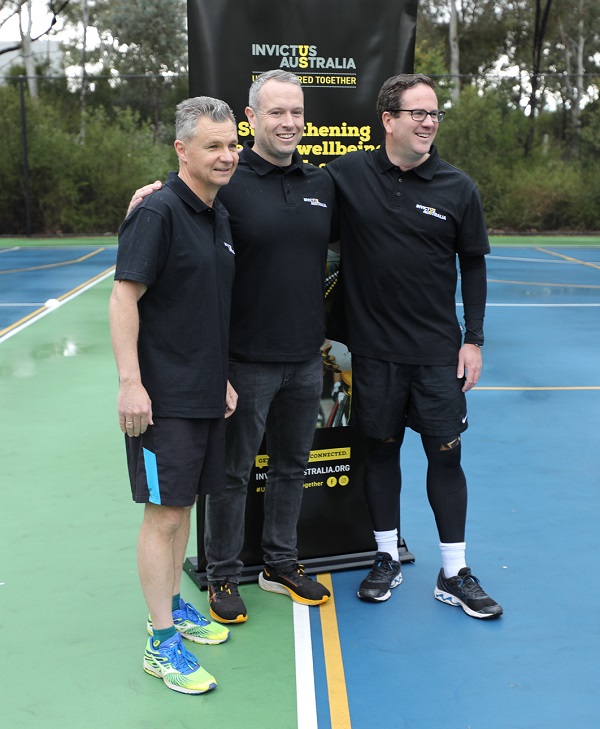 Three men in activewear posing next to Invictus banner