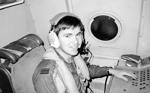 Ian Pearson wearing a headset look at the camera from the cockpit of a P-3C Orion plane.