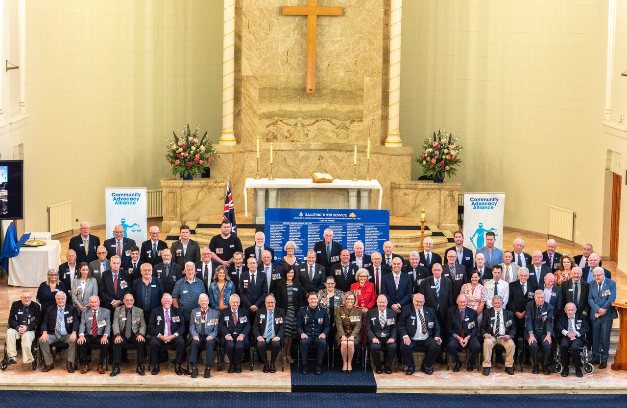 A large group of people seated in the Victoria Police Academy Chapel. There is a large cross in the background.
