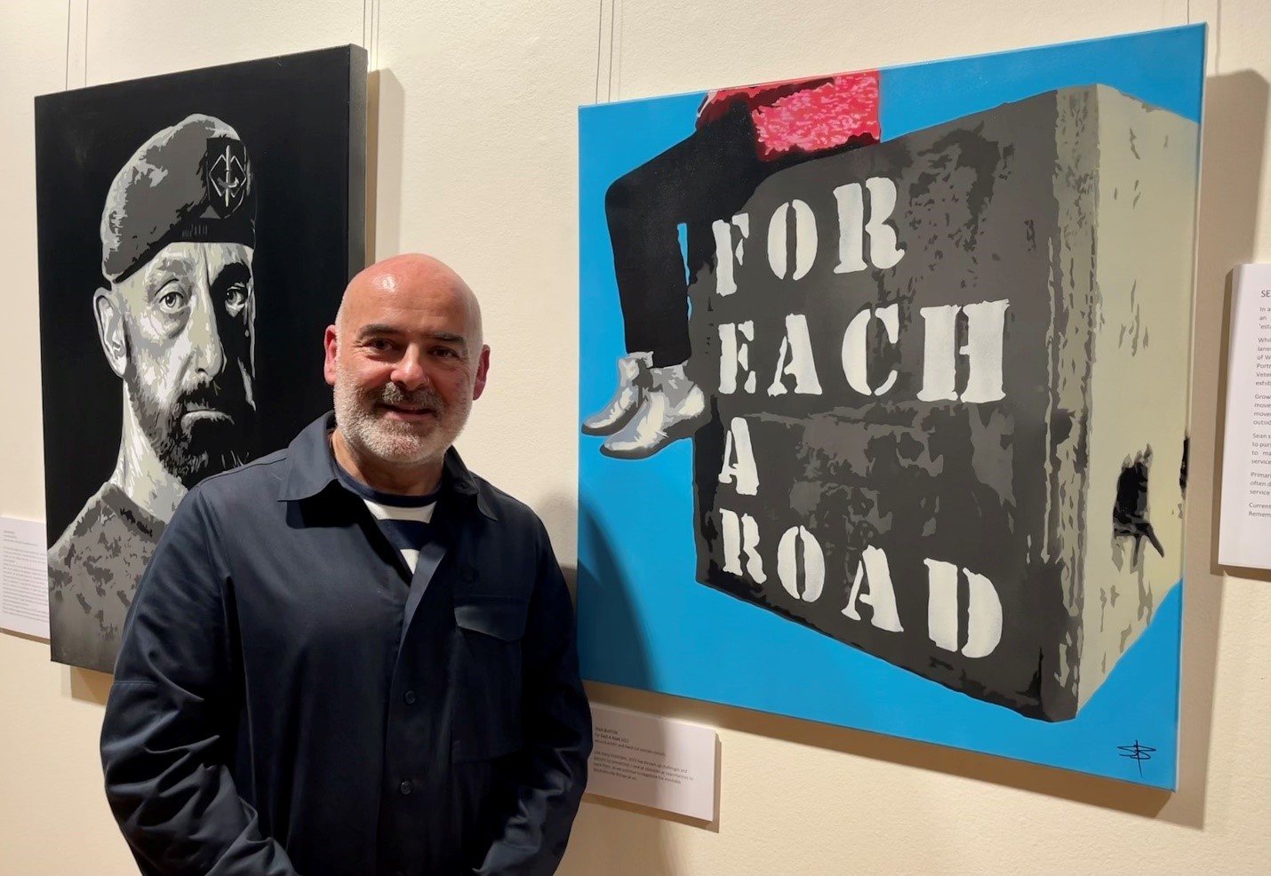 Sean stands in front of two paintings hanging on a wall.