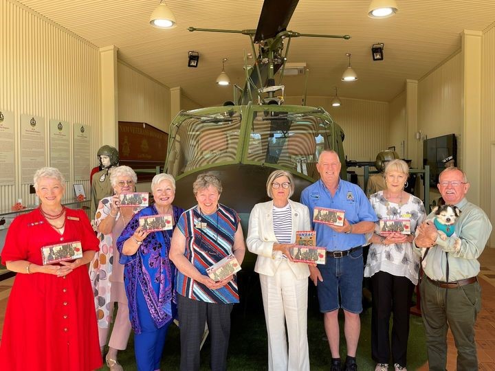 Group of eight people posing in front of Army helicopter in a museum