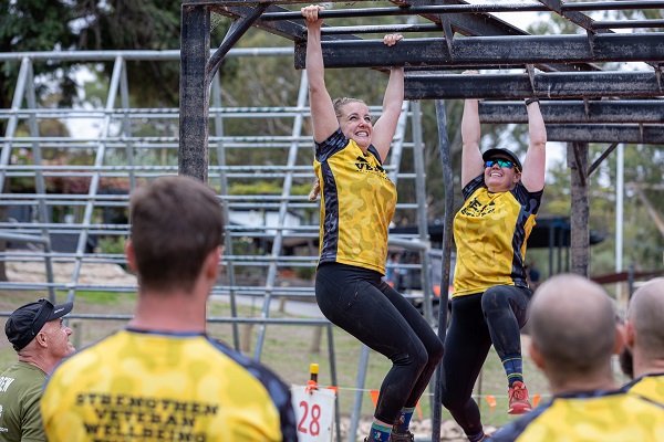 Two people wearing Team Veteran T-shirts on obstacle course, watched by others in their team