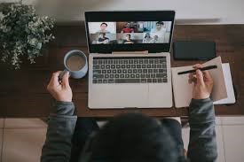 A person in an online conference with coffee on one hands and notes in the other