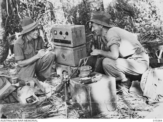 Two men in Army uniform crouching by an old radio in the jungle