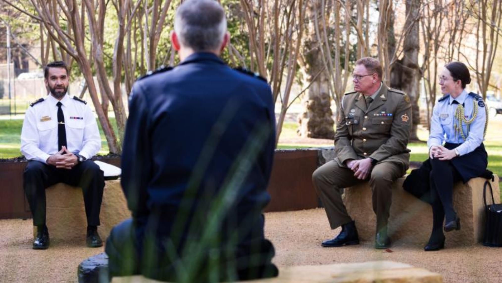 RAAF, Navy and Army personnel chat on seats in open air