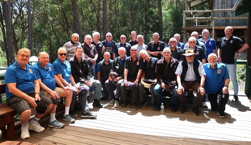 About thirty older men pose for photo on timber deck