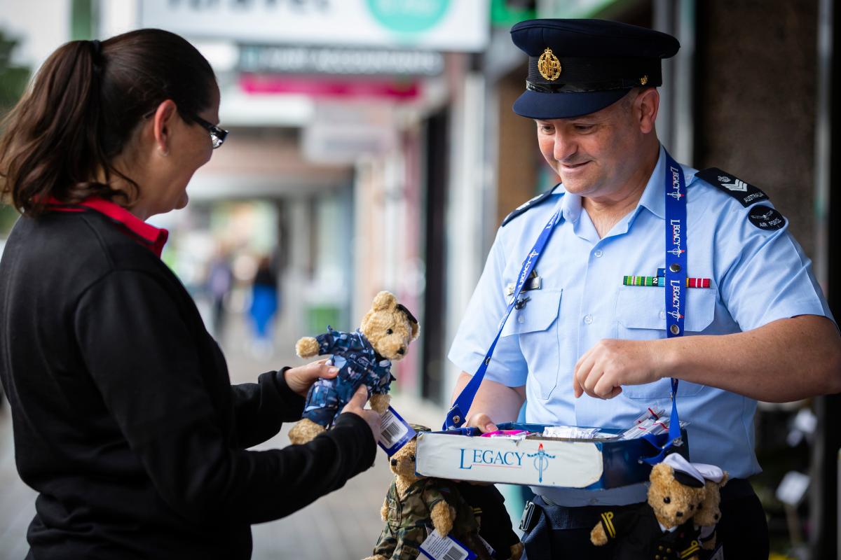 Man in RAAF uniform sells a Legacy bear to a woman