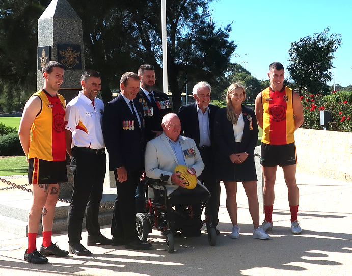 Eight people, including a wheelchair user, posing for camera next to cenotaph