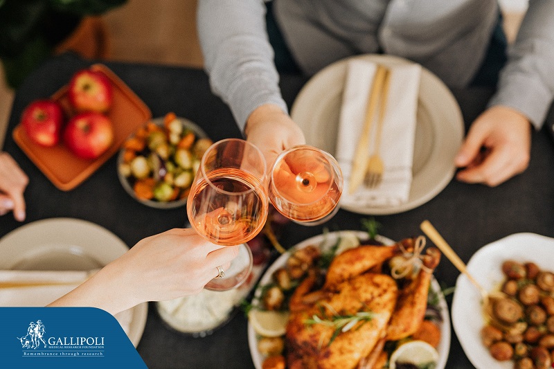 Photo of table covered in food with hands holding glasses of wine