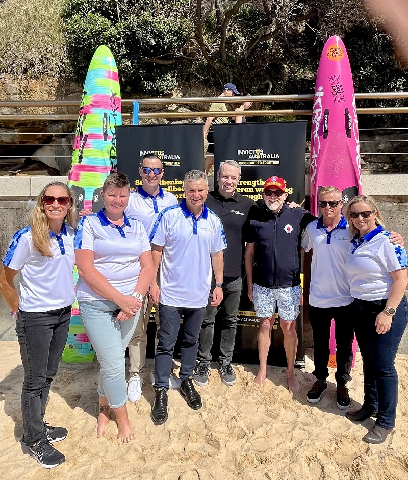 Nine men and women pose on beach in front of Invictus signage
