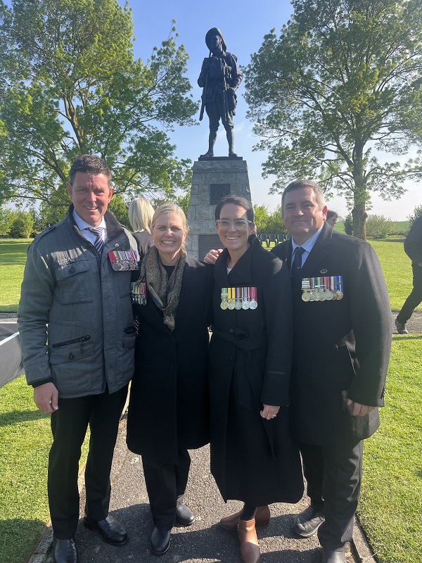 Four people wearing medals posing in front of digger memorial