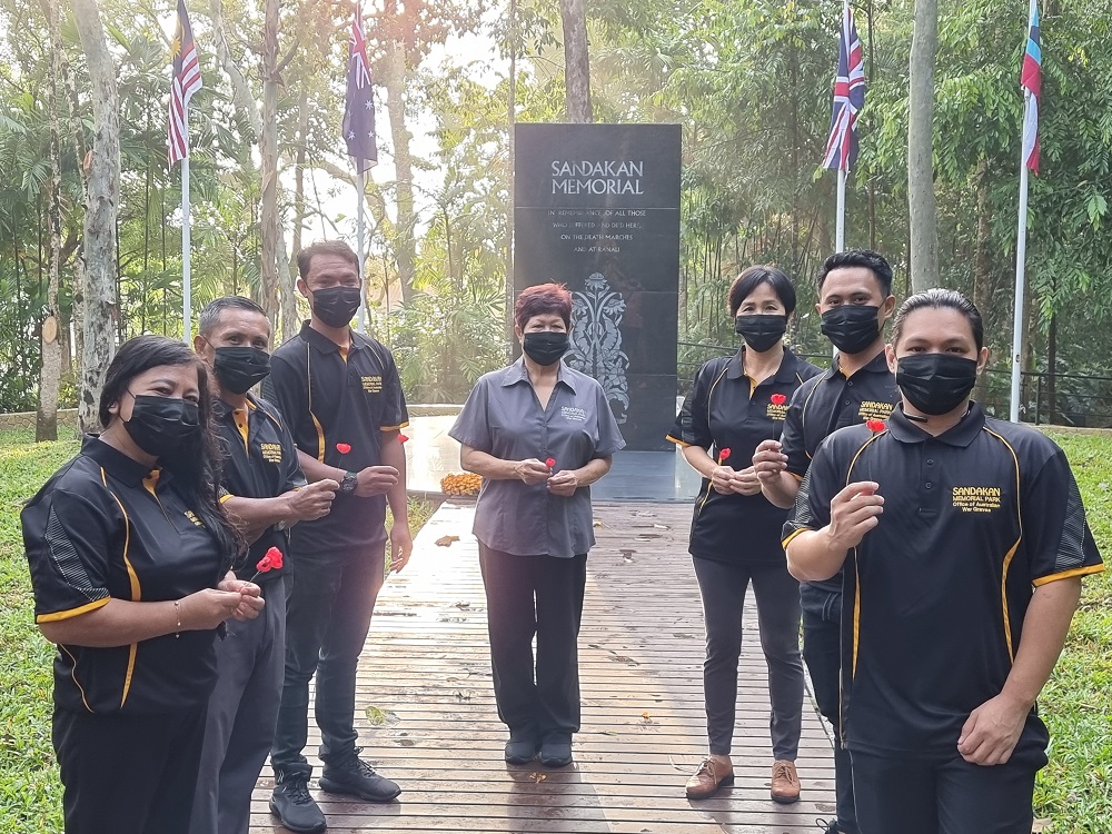Seven Asian people posing in front of black obelisk surrounded by jungle.