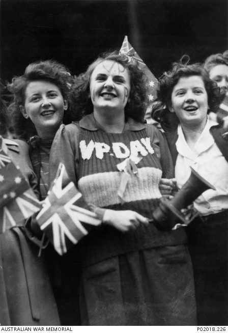Smiling young women crowded together, one with VP Day written on her jumper