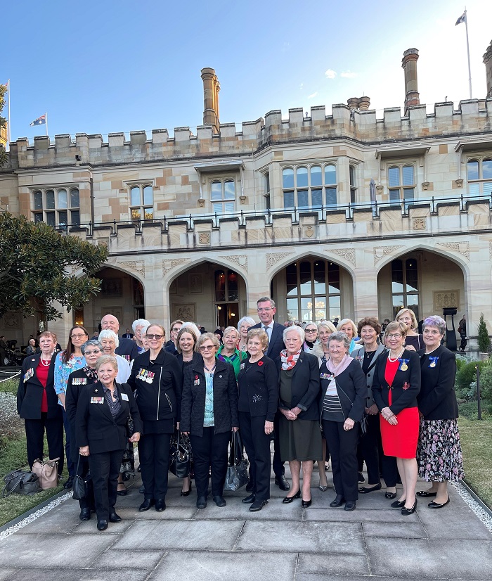 One man and about twenty older women pose for photo outside gothic sandstone house