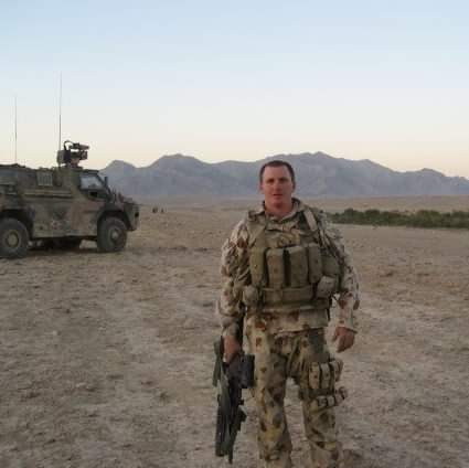 Soldier in front of armoured vehicle in desert.