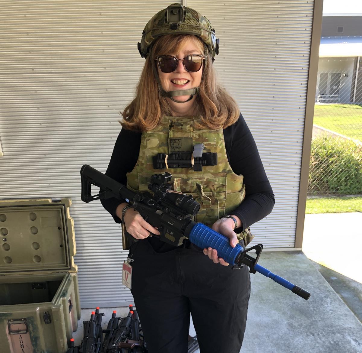 A woman wearing combat gear standing next to a box and guns