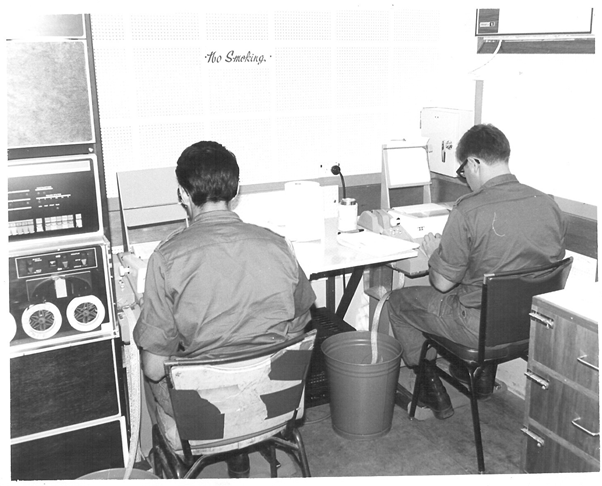 Two young men in uniform seated in front of teleprinters or similar.