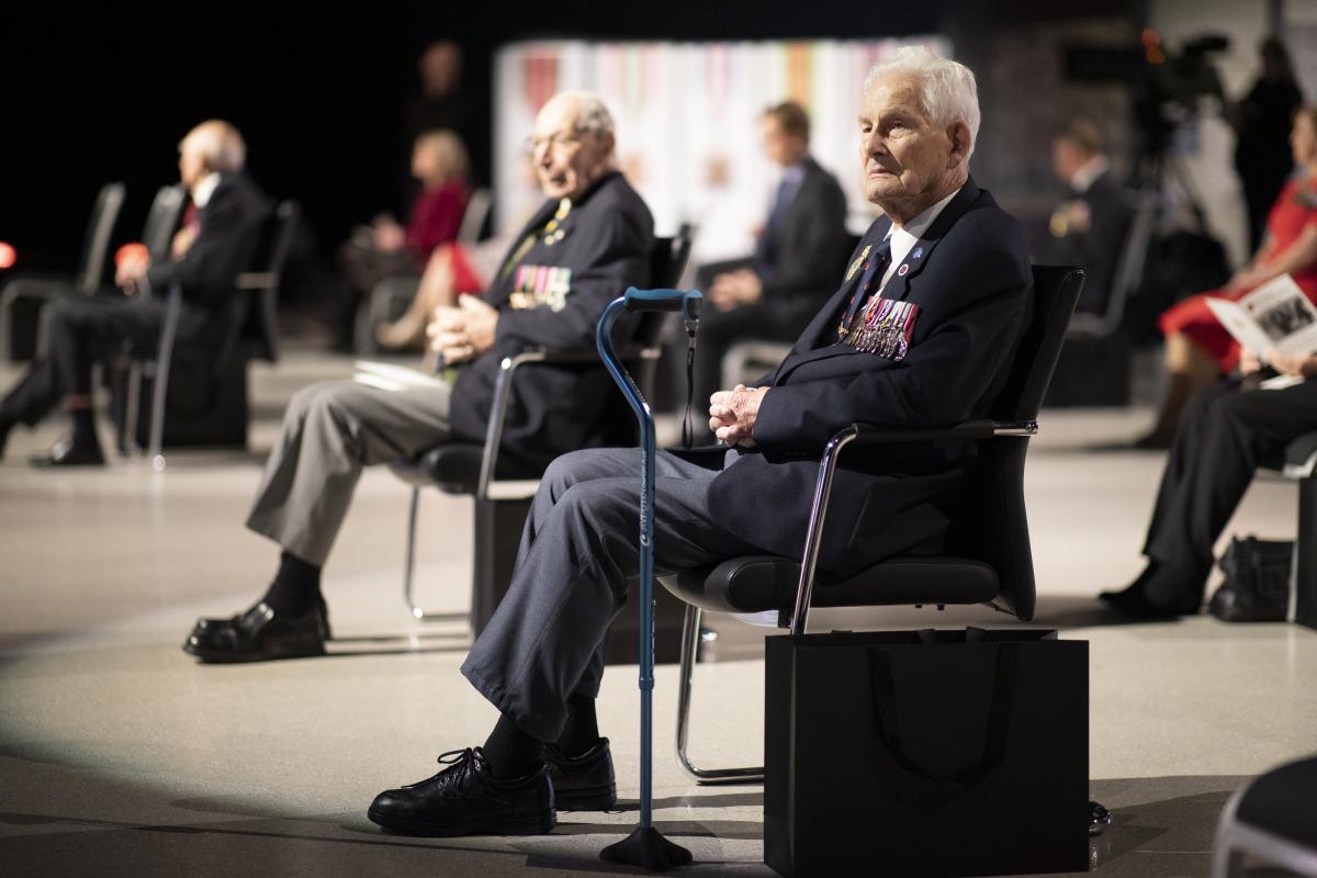 Two elderly men seating with others in the Australian War Memorial’s exhibition hall.