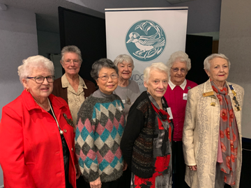 six women posing in front of a War Widows banner.