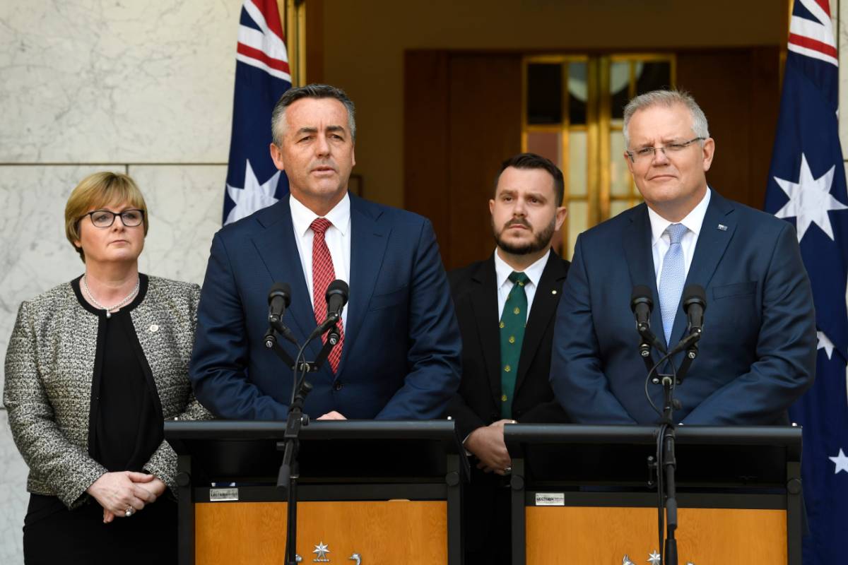 Two middle-aged men in suits stand at lecterns. Behind them are a woman and a man and two Australian flags. They are at Australian Parliament House.