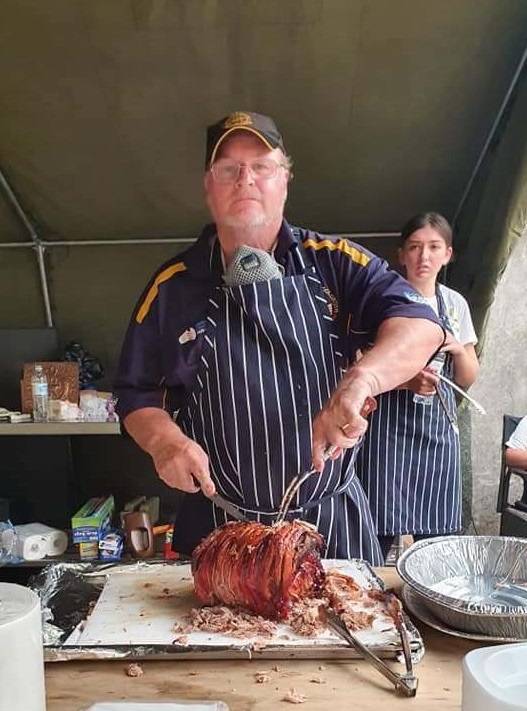 Man in sixties wearing apron carves a roast inside a large tent.