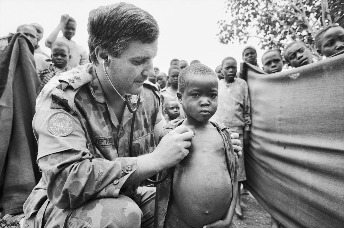 Army doctor treats African child, surrounded by other children.