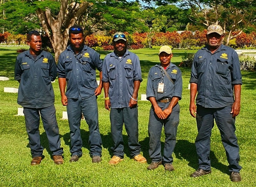 Five Bita Paka War Cemetery staff members all standing in a row at the Bita Paka War Cemetery in Papua New Guinea. They are dressed in their landscaping uniforms.