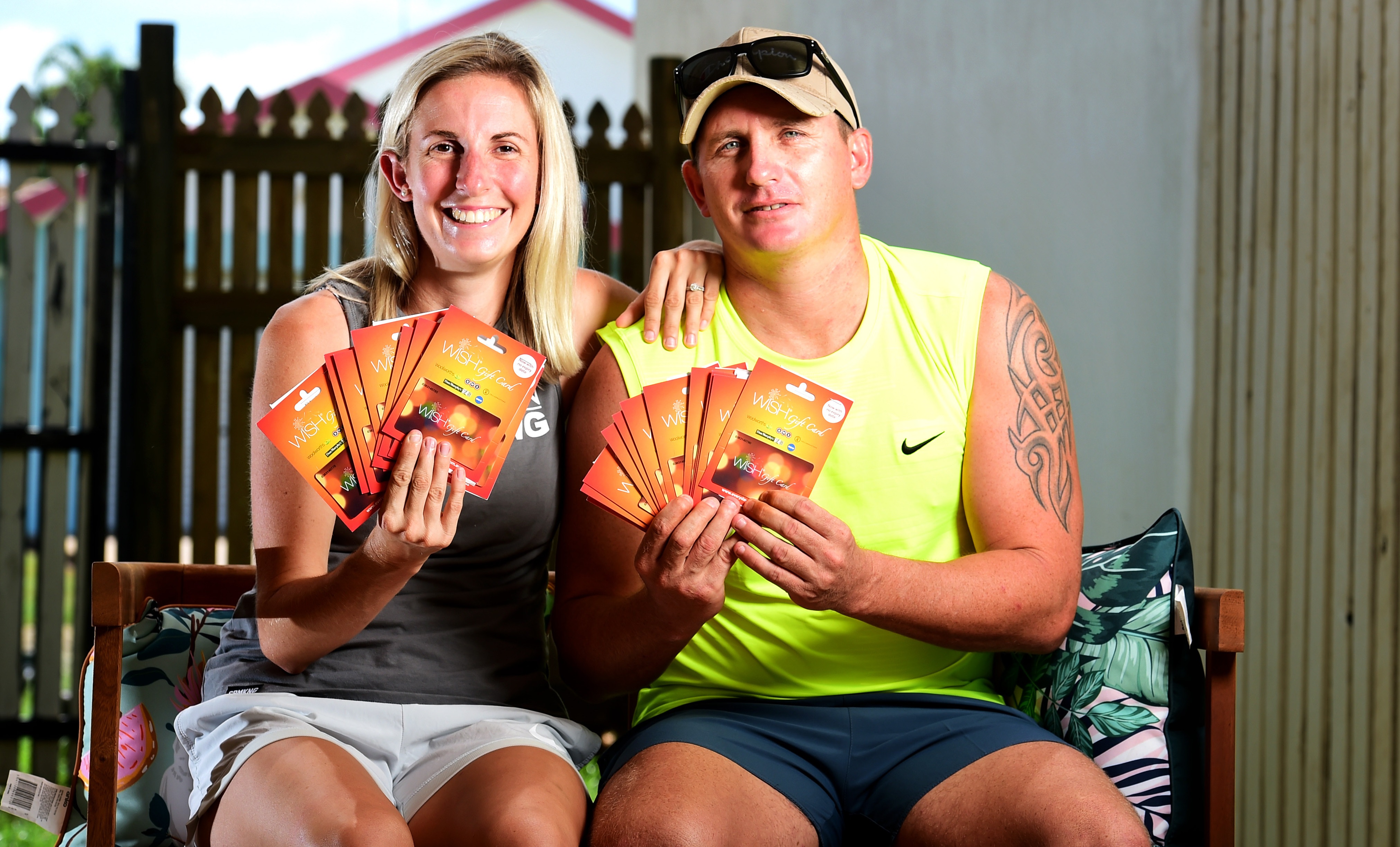 Beau King and Stacey Lyon, sitting down in casual, light clothing. Both are holding fistfuls of supermarket gift cards.