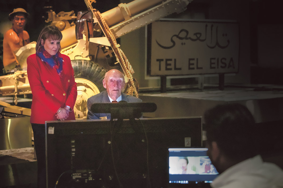 Woman standing next to seated elderly man talking to computer screen
