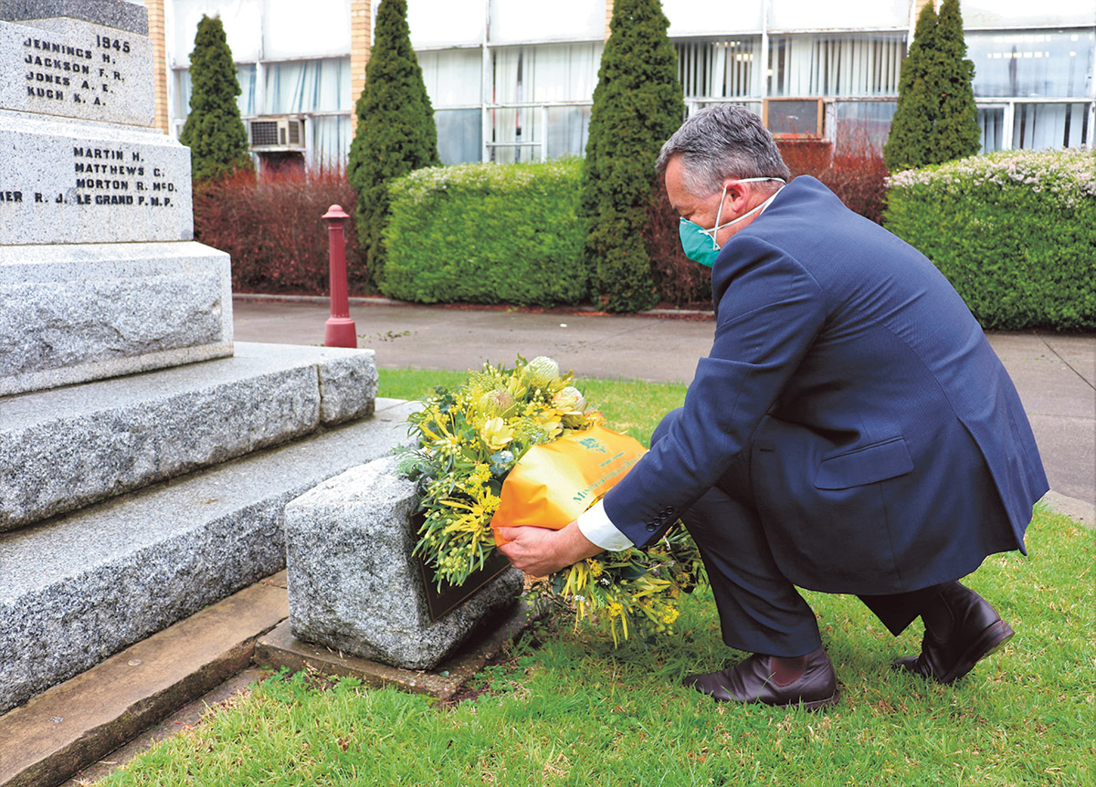 Minister Chester lays wreath at the cenotaph, wearing a blue suit and face mask.
