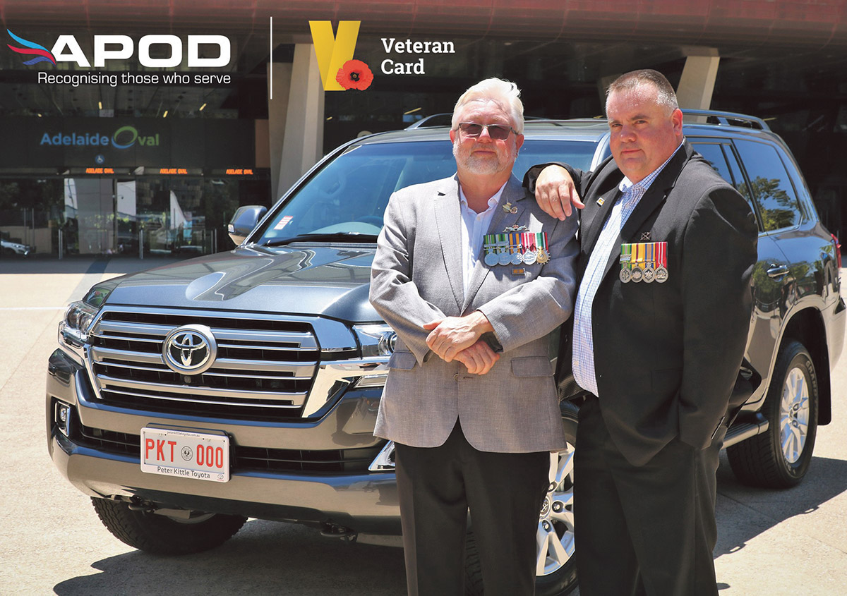 two men wearing medals pose in front of Toyota SUV