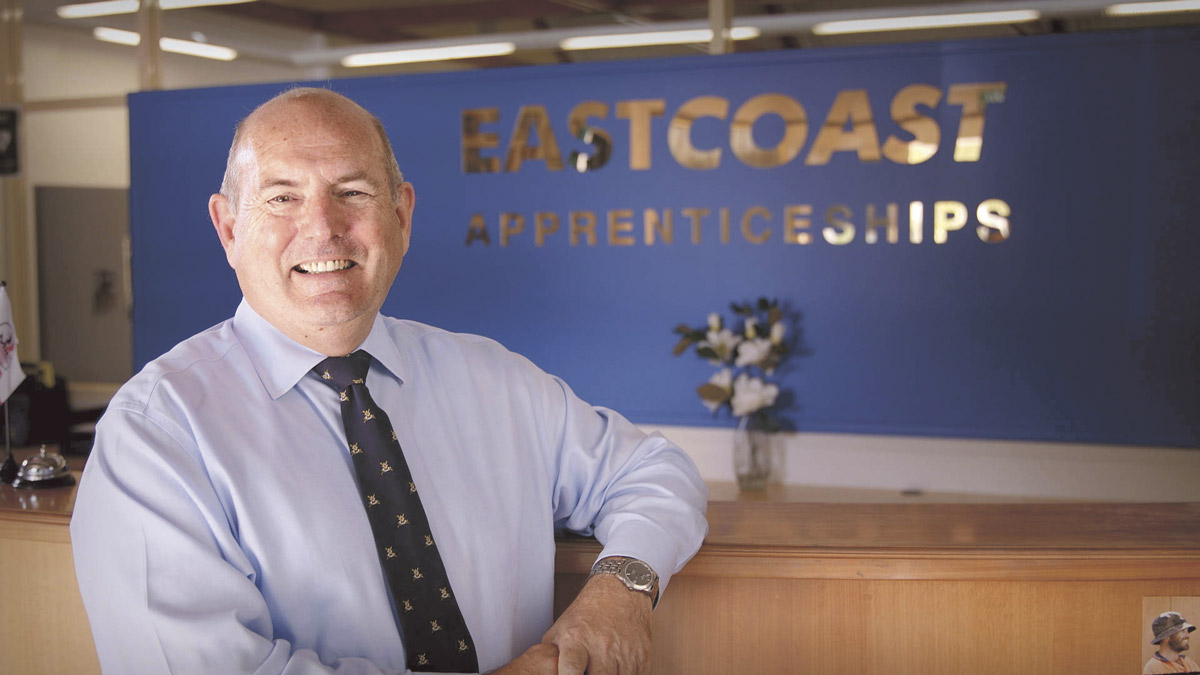 Smiling man leaning on reception desk with Eastcoast Apprenticeships sign in background