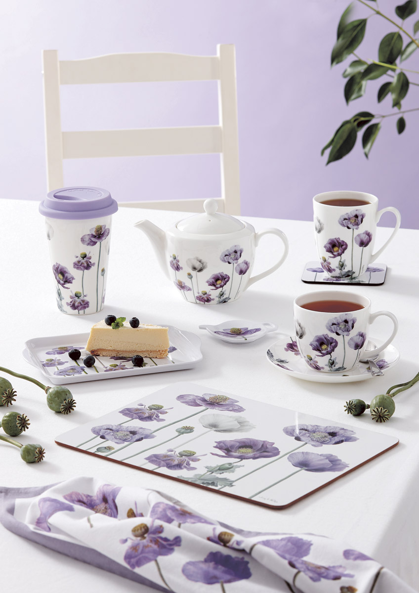 Various cups mugs,  teapots and placemats with a purple poppy pattern, on a table with a white chair