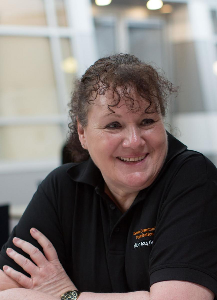 A woman named Viv Lawrence, who works as an ADF Transition Coach. She is sitting down, wearing a black Open Arms t-shirt, with her arms folded and smiling.