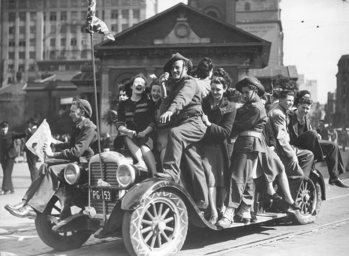 About a dozen servicemen and several civilian women all crowded onto a car, smiling and celebrating Victory in the Pacific Day in Martin Place, Sydney on 15 August 1945.