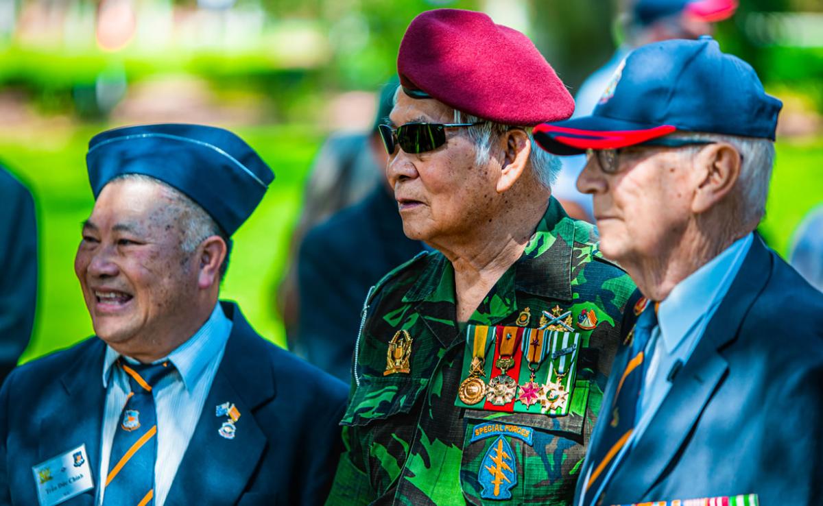 Two South Vietnamese veterans Chin Duc Tran and Ha To Ha with Australian Vietnam veteran Peter Bray AM. Ha To Ha is wearing a camouflage uniform and Chin Duc Tran and Peter Bray are wearing navy suits.
